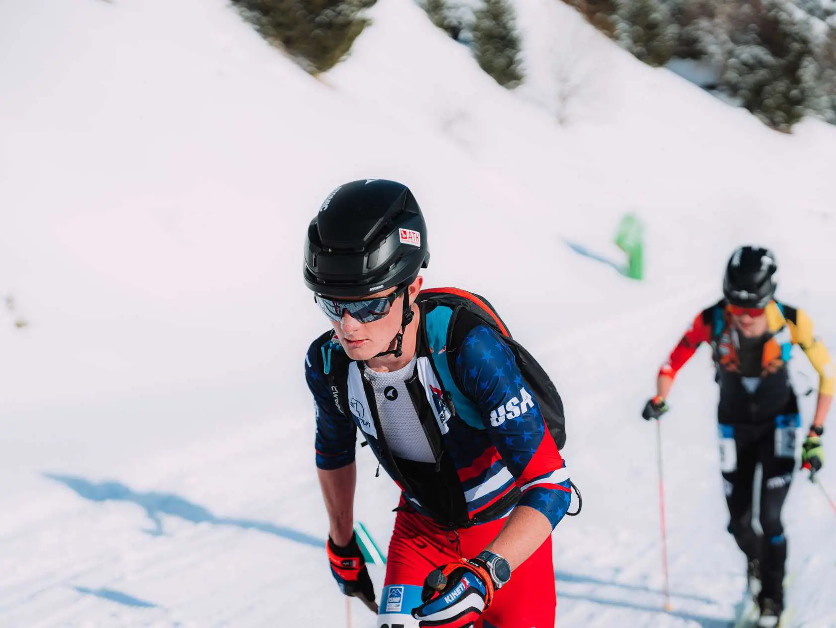 Two men skiing down a snowy hill with trees in the background