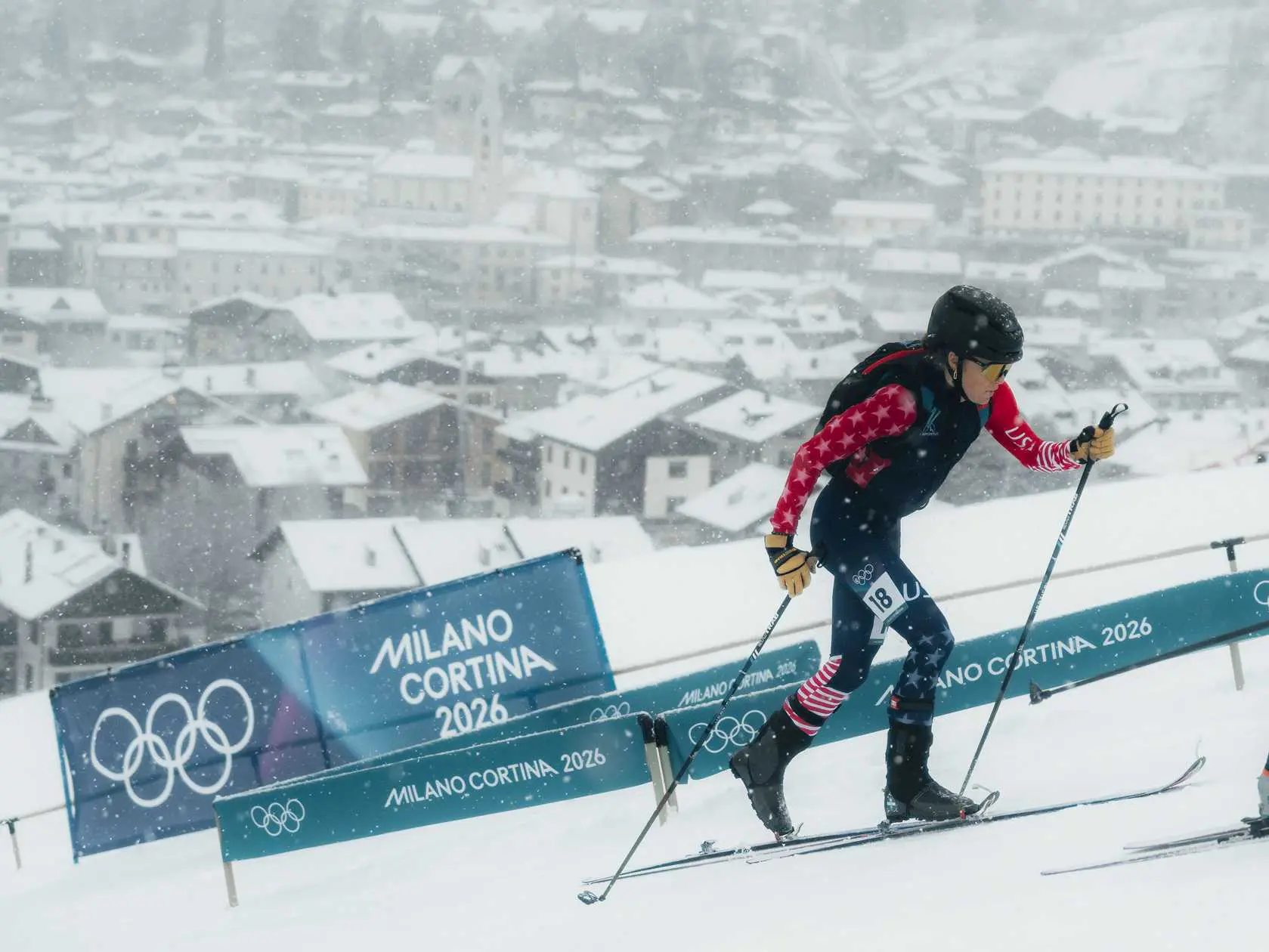 Skier ascending snowy hill, Olympic banners