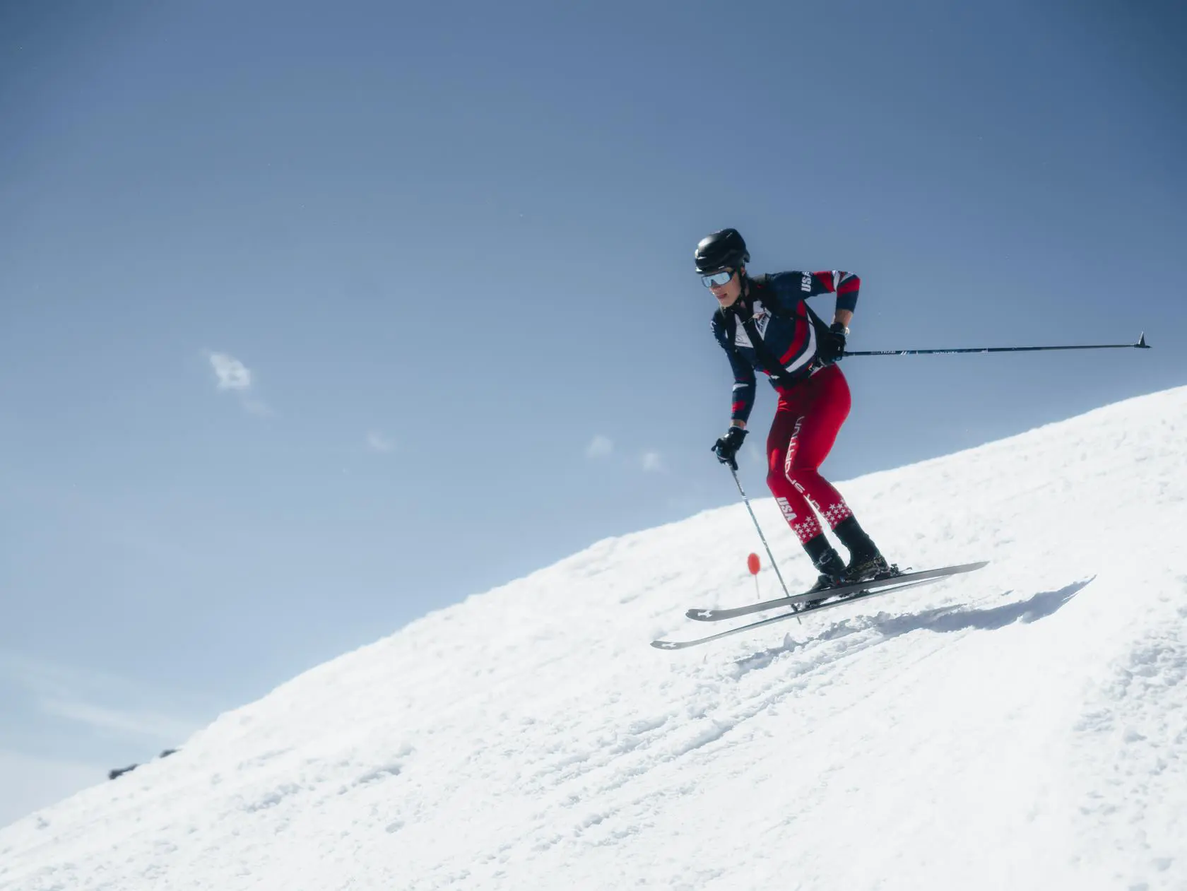 Skier descending snowy slope under blue sky