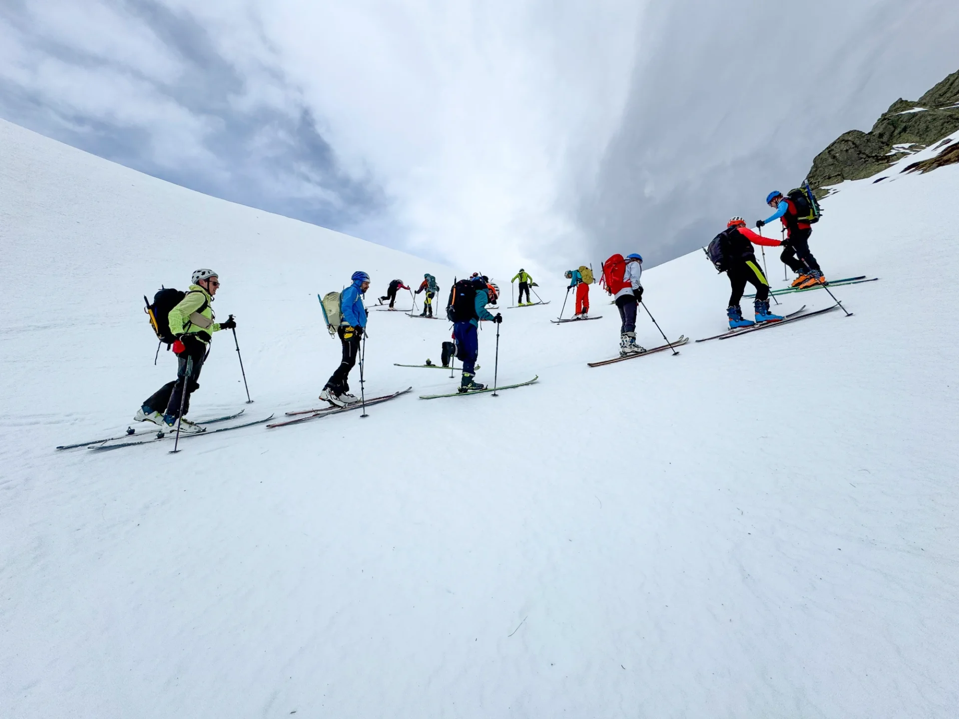 Group of people wearing helmets, bags, and gloves, holding ski poles, and skiing down a snow-covered slope