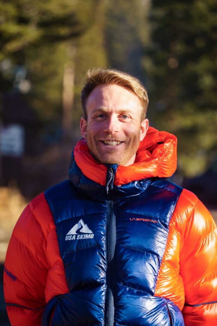 Man in a blue and jacket standing in the snow, He is surrounded by trees in the background