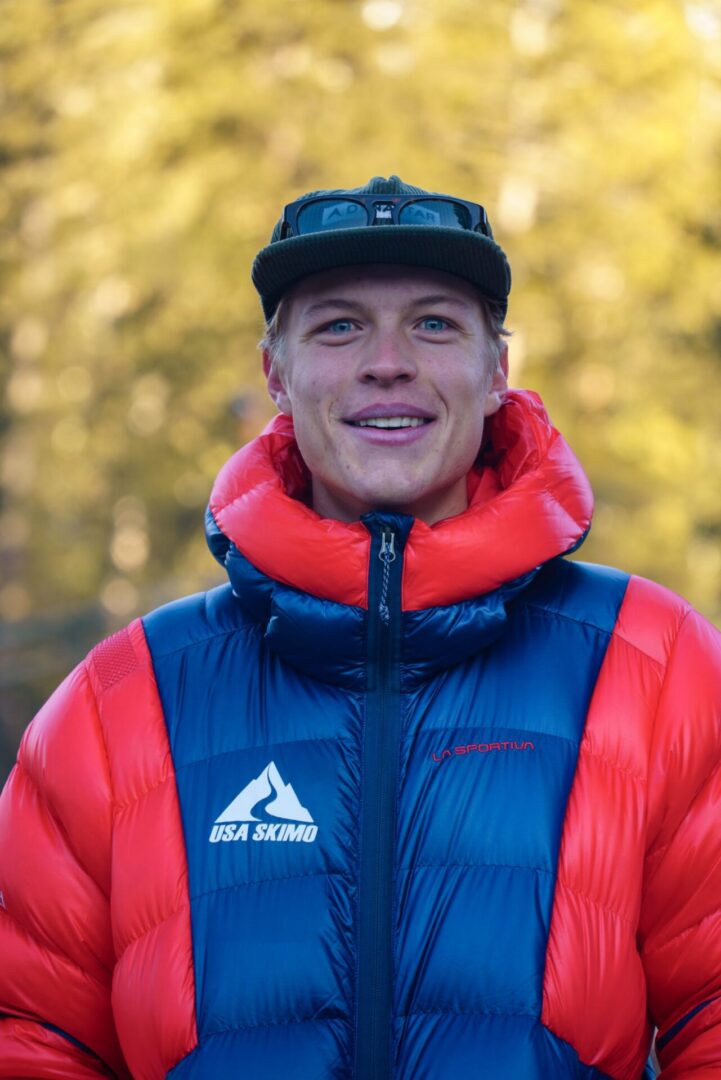 Man in a red and jacket and hat standing in front of a backdrop of trees