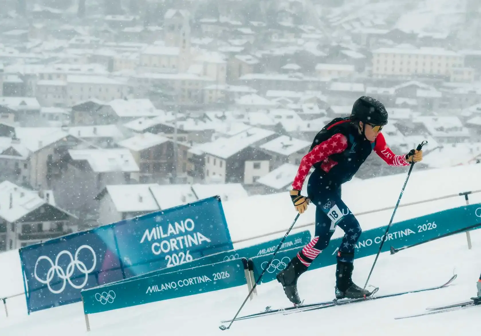 Skier wearing a helmet, goggles, gloves, and shoes, holding ski poles, racing down a snowy slope